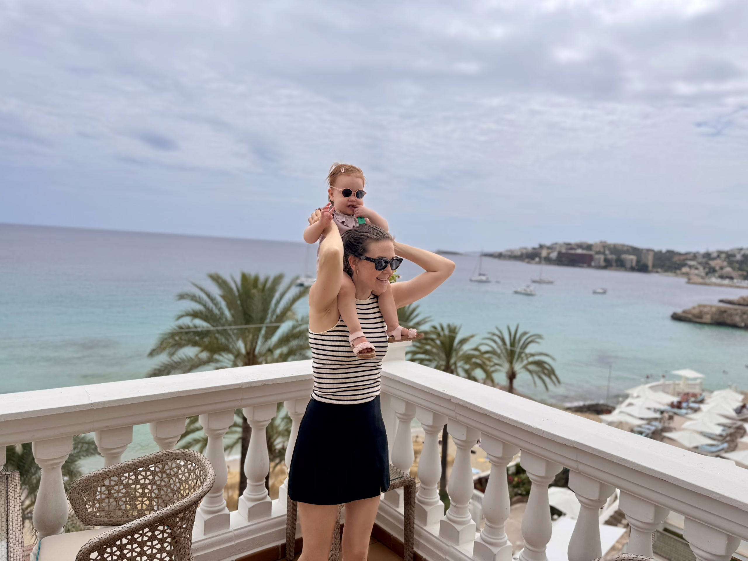 Bilde av vår nyansatt, Julia. Et fotografi av Julia i syden med baby på skuldrene. Julia har på seg en tank top med hvite og svarte striper og et svart skjørt.